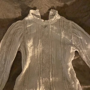 Vit blus - Denna vita blusen säljs för endast 30 kr! Blusen har fint blommigt mönster och passar perfekt i vardags-samt finare sammanhang!