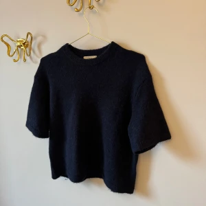 Marinblå stickad tröja från Gina Tricot premium collection - Säljer en mysig mörkblå stickad tröja från Gina Tricot premium collection. Tröjan har en rund halsringning och korta ärmar. Knappt använd så fint skick!