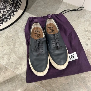 Svarta sneakers från Eytys - Snygga svarta sneakers från Eytys med vit sula och klassisk snörning. Skorna har en stilren design och är perfekta för en avslappnad look. De kommer med en praktisk lila skopåse.