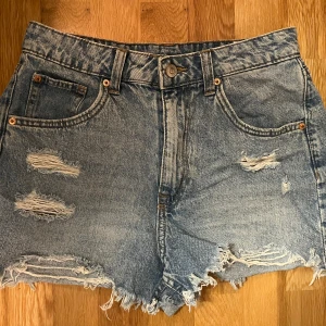 Blå jeansshorts - Säljer ett par blå högmidjade jeansshorts med slitna detaljer. Knappt använda o säljer på grund av att de inte passar mig längre o är inte min stil.
