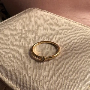 Guldfärgad ring med hjärtdetalj - Elegant guldfärgad ring med en liten hjärtdetalj framtill. Perfekt för att ge en subtil men stilfull touch till din look. Passar bra till både vardag och speciella tillfällen. Från Pandora!! Säljer för att jag fick i present men inte är guldtjej!