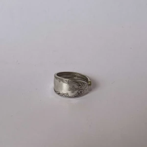 Silverfärgad ring med gravyr - Elegant silverfärgad ring med vacker gravyrdetalj. Perfekt för att ge en stilfull touch till din outfit. Ringen har en bred design som gör den till ett iögonfallande smycke.