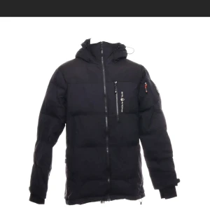 Svart dunjacka från Sail Racing - Snygg svart dunjacka från Sail Racing med dragkedja och huva. Jackan har en praktisk bröstficka med dragkedja och en logga på ärmen. Perfekt för kyliga dagar.