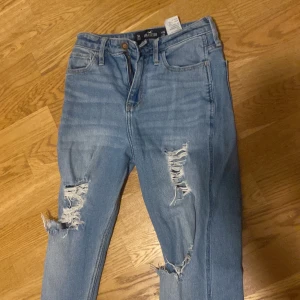 Blå jeans med slitningar - Säljer ett par blå jeans med coola slitningar på framsidan. De har en klassisk femficksdesign och knappgylf. Perfekta för en avslappnad stil.
