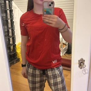 Röd t-shirt från Nike - Säljer en röd t-shirt från Nike med korta ärmar och en vit Nike-logga på bröstet. Perfekt för träning eller vardagsbruk. T-shirten är liten i storleken och är gjord i ett bekvämt material. Den har också svarta streck bak på tröjan som inte går bort i tvätt, och initialerna RV från fotboll.