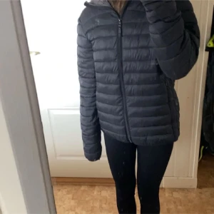 Svart dunjacka med dragkedja - Säljer en svart dunjacka med dragkedja och huva. Den är använd en del men bra skick bara att den har jätte små hål på ryggen som knappt syns (se bild) köpte för 400kr i strl s men passar xs