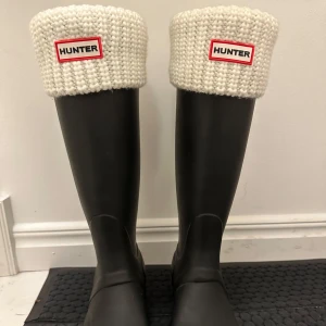 Svarta gummistövlar från Hunter - Säljer ett par klassiska svarta stövlar från Hunter med justerbara spännen tillsammans med vita hunderstrumpor. Strumporna går att ta ut från stövlarna om man inte vill ha dom i.