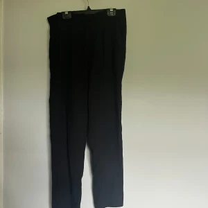 Svarta kostymbyxor från Amisu - Svarta kostymbyxor från Amisu i klassisk rak modell. Byxorna har hög midja och stängs med dragkedja och knapp. Perfekta för en clean och stilren look. Materialet känns mjukt och följsamt.