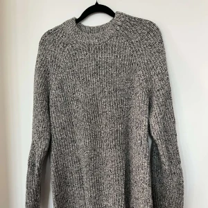 Grå stickad tröja från 157 - Säljer en chunky gråmelerad stickad tröja från 157. Tröjan har en hög, ribbad halsringning och långa ärmar. Perfekt för lager-på-lager och riktigt skön att mysa i under kyliga dagar.