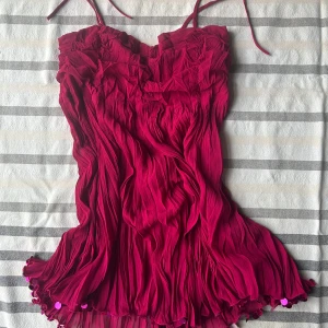 Rosa plisserad linnetopp med paljetter - Supersöt rosa linnetopp med plisserat tyg och smala axelband som knyts. Toppen har volangig nederkant dekorerad med glansiga paljetter 🩷