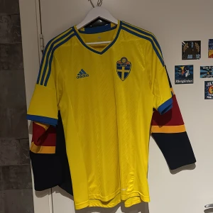 Svenska landslagets fotbollströja Adidas - Gul fotbollströja från Adidas med blå detaljer och Sveriges landslagsemblem på bröstet. Klassisk V-ringning, blå ränder på axlarna och Adidas-logga. Tillverkad i lätt och ventilerande material, 