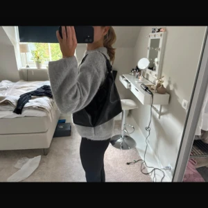 Svart axelväska i skinn med dragkedja - Säljer en svart axelväska i mjukt skinn med snygg, lite slouchy form. Väskan har en bred axelrem med knutdetaljer och stängs med dragkedja i guld. Perfekt storlek för att få plats med allt du behöver till vardagen.