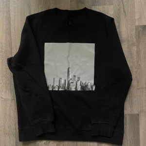 Svart sweater H&M - Svart sweatshirt från H&M i storlek L med en stor gråvit print av en stadssilhuett på bröstet. Perfekt för dig som gillar stilrena och urbana vibes.