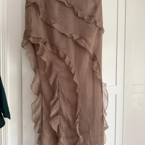 Brun volangkjol från H&M - Säljer en lång, brun kjol från H&M i transparent och lätt material. Kjolen har flera volangdetaljer. 