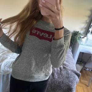 Grå Levi's sweatshirt med röd logga XS - Säljer en grå sweatshirt från Levi's i storlek XS. Tröjan har en klassisk röd Levi's-logga framtill, rund halsringning och långa ärmar. Mjuk och skön bomullsblandning, perfekt till jeans eller leggings. Enkel och stilren design som funkar året runt.