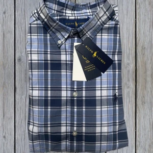 Blårutig skjorta från Ralph Lauren - Helt ny stilren blårutig skjorta från Ralph Lauren med klassisk krage och knappar framtill. Skick 10/10 | Skjortan är i barnstorlek XL (170) vilket motsvarar S i vanlig storlek. Säljer eftersom den inte passar, skjortan är köpt för ca 1000kr | Tveka inte att höra av er vid minsta funderingar!