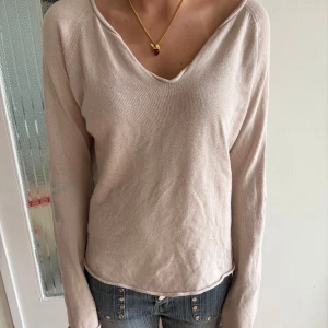 Rosa stickad tröja Hunkydory - Ljusrosa stickad tröja från Hunkydory Essentials med v-ringning och långa ärmar. Tröjan har diskreta stjärndetaljer på armbågarna och en avslappnad passform. Perfekt för lager-på-lager och enkel att styla med jeans.