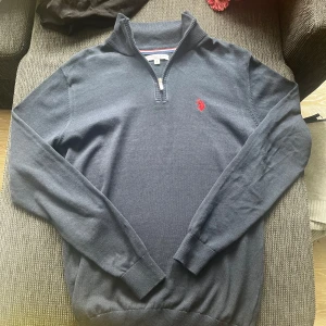 Mörkblå half zip tröja US Polo Assn - Mörkblå långärmad tröja från US Polo Assn med halv dragkedja och röd broderad logga på bröstet. Tröjan har ribbade muddar och krage, perfekt för lager-på-lager. Materialet är mjuk bomull som känns skönt mot huden. Nypris ca 530
