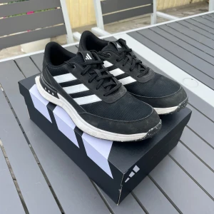 Svarta Adidas golfskor - Snygga svarta Adidas golfskor med klassiska vita ränder på sidorna. Endast använda ett fåtal gånger då de köptes i slutet av förra golfsäsongen. Storlrk 41 1/3, passar 41 och 42 bra. Nypris 1500kr. Box medföljer‼️