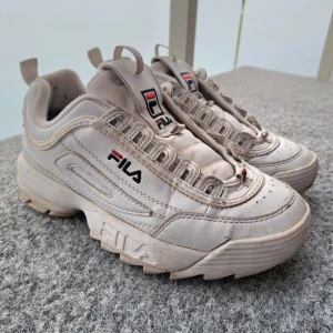 Vita Fila Disruptor sneakers strl 39 - Chunky vita Fila Disruptor sneakers med grov sula och klassisk logga på sidan och plösen. Skorna har snörning och är tillverkade i syntetmaterial med textilfoder. Perfekta för dig som gillar retrostil och streetwear.