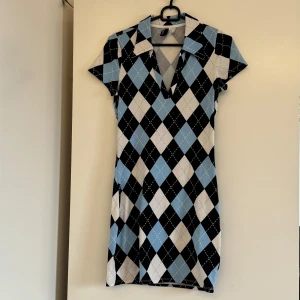 Rutig kortklänning från H&M - • Endast använd 1-3 gånger. Säljer då jag bytt stil.  • Supersöt kortklänning från H&M med blå, vita och svarta rutor i ett klassiskt argylemönster.         • Klänningen har krage, v-ringning och korta ärmar. 