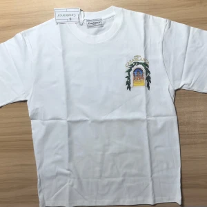 Vit Casablanca t-shirt med tryck - Vit t-shirt från Casablanca med färgglatt tryck av en byggnad och gröna blad både fram och bak. Stort 'Avenida Casablanca'-motiv på ryggen. Klassisk passform och rund hals. Perfekt för dig som gillar snygga statement-plagg. Storlek är L men passar som M. Vid minsta fundering skicka dm:)