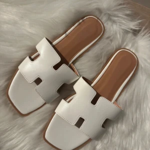 Vita sandaler med fyrkantig tå - Stilrena vita sandaler med bred rem i skinnimitation och fyrkantig tå. Kopior. Kan upplevas lite stora men det är storlek 39 oavsett vad som står under tofflan. Aldrig använda. 