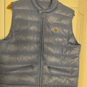 Moncler väst - Snygg ljusblå Moncler väst . Västen har dragkedja framtill, två fickor med dragkedja och klassisk Moncler-logga på bröstet.