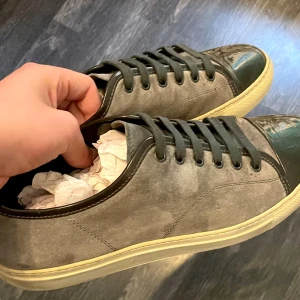 Gråa Lanvins  - Snygga Lanvins i grå mocka med svarta snören och lackad svart tå. Skorna har en vit sula som ger en klassisk look och passar perfekt till en trendig look. Runda tår och platt sula för en avslappnad vibe.