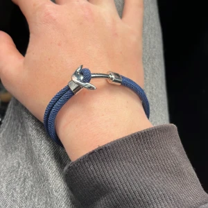 Blått armband med silverfärgat ankare - Säljer ett snyggt armband med blått rep och ett silverfärgat ankare som lås. Perfekt accessoar för dig som gillar marina detaljer och stilren design. Armbandet har en cool och avslappnad vibe.