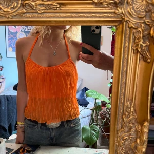 Orange halterneck-linne - Orange halterneck topp i plisserat tyg med lite paljetter i (se sista bilden). Står varken märke eller storlek i då lappen är borta men skulle säga xs/s! 