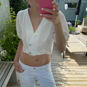 Vit croppad blus från Zara - Superfin vit croppad blus från Zara med puffiga korta ärmar och djup v-ringning. Blusen har två dekorativa knappar framtill och är gjord i ett lätt bomullstyg. Lappen är kvar, aldrig använd.