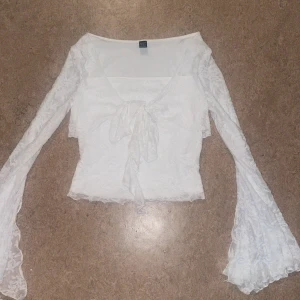 Vit spetsblus med knut.  - Supersöt vit blus från SHEIN i spets med långa utsvängda ärmar och stor knytrosett framtill. Blusen har v-ringning och transparenta detaljer som ger en romantisk vibe. Aldrig använd säljer eftersom jag hitta en annan tröja 