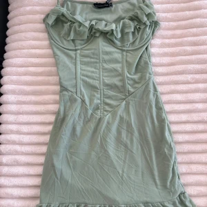 Ljusgrön kort klänning med volang - Supersöt ljusgrön kort klänning från PrettyLittleThing med smala axelband, volangdetalj vid bysten och figurnära passform. Oanvänd med prislappen kvar. 