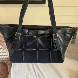  axelväska  - Snygg mörkblå axelväska från Ripani i skinn med detaljer i mocka på framsidan och dekorativ rosett. Väskan har guldiga spännen, dragkedja upptill och flera innerfack. Perfekt storlek för att få plats med allt du behöver till vardagen.❤️ 