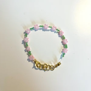 Pärlarmband med rosa blommor - Supergulligt armband med små rosa pärlblommor och gröna pärlor mellan varje blomma. Armbandet har ett justerbart guldfärgat lås. 13,5-15,5 cm. 35kr+ frakt =57kr. Tar bara swish. TikTok: jewelrybysara13
