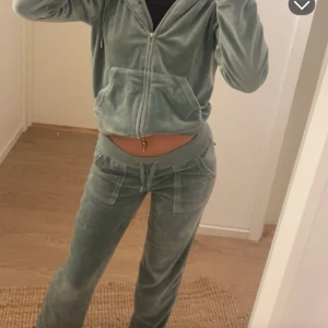 Grönt juicyset - Snygga gröna mjukisbyxor i mjuk velour med låg midja och snörning i midjan. Byxorna har raka ben och fickor både fram och bak, bakfickorna har lock med knappar. Perfekta för en chill och avslappnad stil.