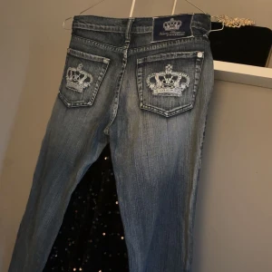 Blåa jeansbyxor med broderade kronor - Snygga blå jeansbyxor från Von Dutch med slitningseffekt och broderade kronor på bakfickorna. 