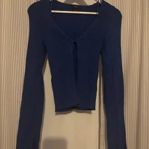 Blå ribbad topp från Lindex - Säljer en blå ribbad stickad topp/kofta från Lindex med långa ärmar som har slits på slutet och är figursydd i midjan. Använd en gång. 