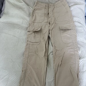 Beiga cargopants från Zara - Snygga beiga cargopants från Zara med stora fickor på sidorna och klassisk cargostil. Byxorna har normal passform, dragkedja och knapp framtill samt bälteshällor. Perfekta för en chill och trendig look.