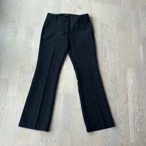 Svarta kostymbyxor med bootcut - Snygga svarta kostymbyxor med bootcut-snitt och pressveck. Byxorna har hällor för bälte och fickor fram, vilket ger en clean och stilren look. Säljer pga att de är för korta. Nypris 499kr