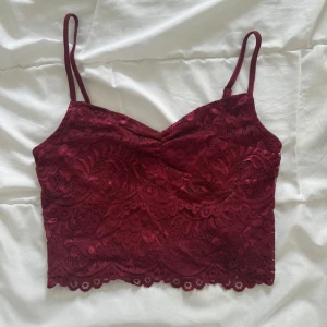 Vinröd spetslinnetopp från FB Sister - Supersnygg vinröd linnetopp från FB Sister med tunna axelband och vacker spets över hela toppen. Croppad modell med blommigt spetsmönster och lätt v-ringning. Perfekt att styla med höga jeans eller kjol för en trendig look