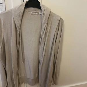 Beige hoodie från 157 i XL - En stilren beige hoodie från 157 i storlek XL. Tröjan har huva med snörning och långa ärmar. Tillverkad i mjukt bomullsmaterial och passar perfekt för en chill och avslappnad look. Enkel design utan tryck eller mönster.