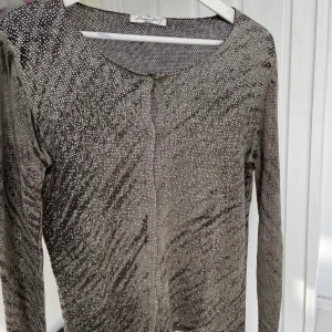 Glittrig kofta från Barbara Lebek - Supersnygg glittrig kofta från Barbara Lebek i silver och svart. Långärmad och med diskret knäppning framtill. Perfekt för dig som vill sticka ut med en elegant och trendig look. Materialet är stickat och känns lätt och bekvämt.