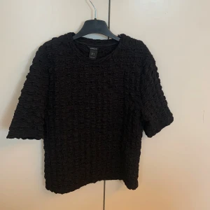 Svart strukturerad topp från Lindex - Svart topp från Lindex med unik strukturerad yta och korta ärmar.