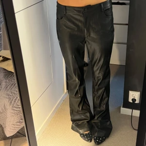 Svarta byxor i skinnimitation - Säljer ett par svarta byxor i skinnimitation från Amisu, storlek 44. Byxorna har en rak och lite vidare passform med klassiska fickor och hällor för bälte. Snyggt glansigt material som ger en edgy look. Sitter perfekt lowwaist på en M/L. OBS notera deffekterna på bild 3/4
