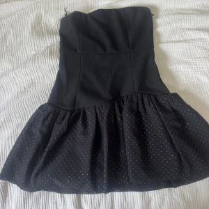 Svart  klänning från Maje - Supersöt svart axelbandslös kort klänning från Maje med volangkjol i transparent tyg med små vita prickar. 