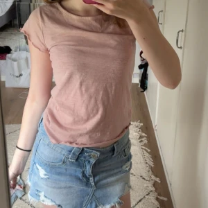 Ljusrosa topp från Lager 157 - Supersöt ljusrosa topp från Angelology i storlek XS. T-shirten har korta ärmar med vågig kant och rund halsringning. Tunt och mjukt material som känns skönt mot huden, perfekt för varma dagar.