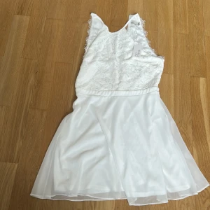 Vit spetsklänning från NLY Trend - Superfin vit kortklänning från NLY Trend med spets upptill och lätt utställd kjol i tunt tyg. Klänningen är ärmlös med v-ringning i ryggen och har snygga fransiga kanter vid axlarna. Aldrig använd och nypris är 499 och i och med att den är oanvänd så säljer jag för 449kr