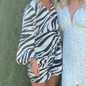 Zebramönstrad kortklänning med puffärm - Säljer en supercool kort klänning med zebramönster i svart och vitt. Klänningen har långa puffärmar och en snygg omlott-look vid kjolen. Perfekt för dig som vill sticka ut och älskar djurmönster!